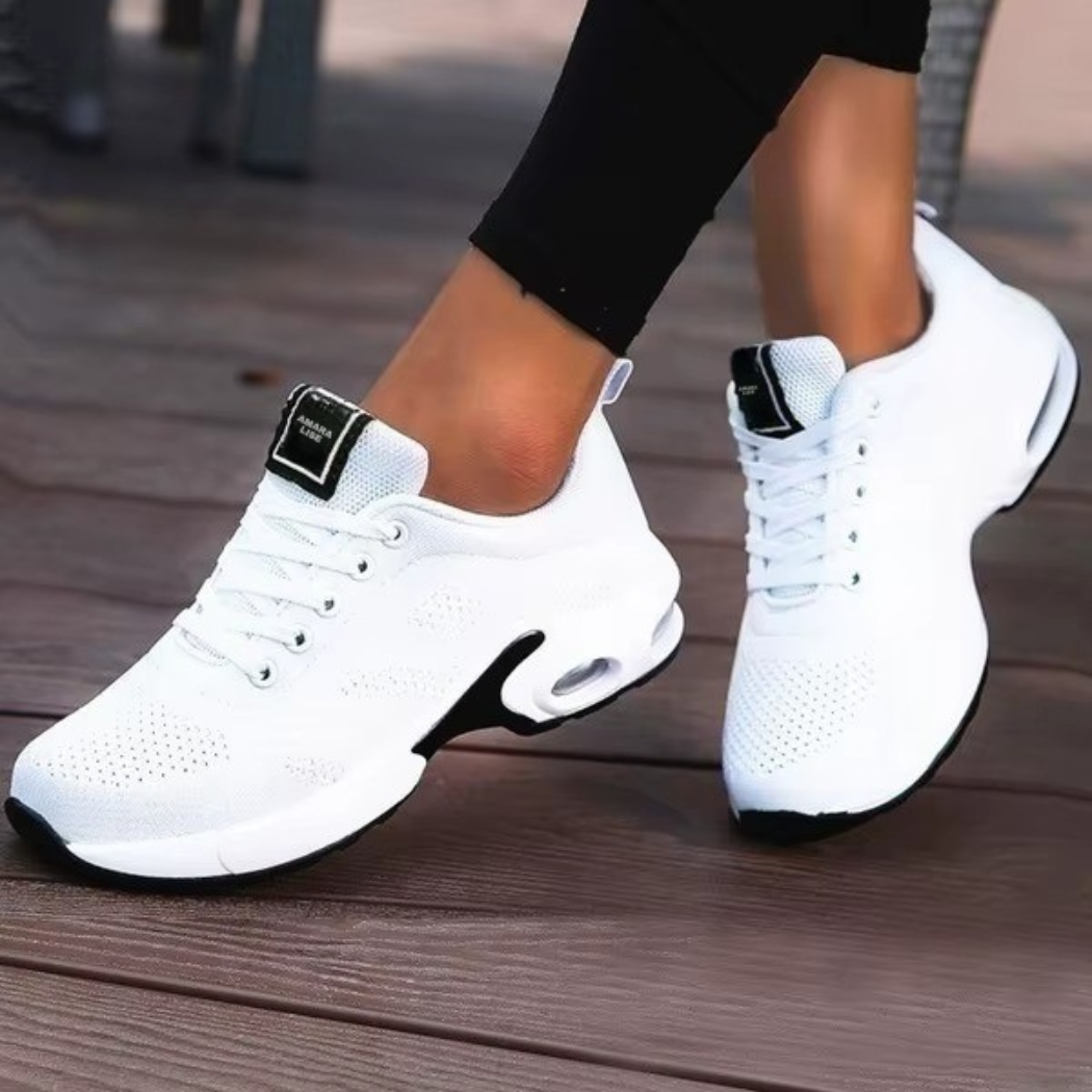 Women’s all-white breathable knit trainers with black sole detail and air cushioned heel, worn on wooden decking.