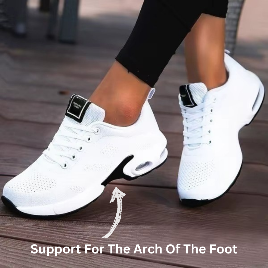 Women’s all-white breathable knit trainers with black sole detail and air cushioned heel with arrows, worn on wooden decking.